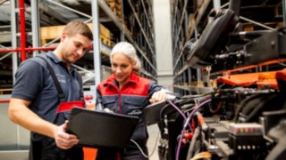 Dwóch techników serwisowych Linde Material Handling patrzy na laptopa obok wózka widłowego.