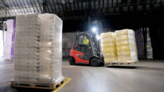 Wózek widłowy gazowy H20 – nowa generacja Wózek widłowy firmy Linde przewozi ładunek w słabo oświetlonej hali, wykorzystując własne oświetlenie