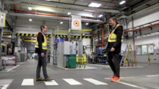 Dwóch pracowników spotyka się w magazynie, nosząc kamizelkę Linde Secure Distance Vest i sygnalizator Linde Distance Beeper.