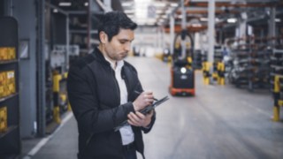 Pracownik firmy Linde Material Handling stoi w magazynie i robi notatki na tablecie.