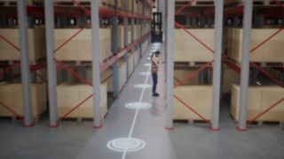 Animacja przedstawiająca pracownika w kamizelce ochronnej w magazynie z wąskimi korytarzami oraz strefy bezpieczeństwa dla rozpoznawania osób.