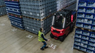 Linde Reverse Assist Radar zmniejsza ryzyko wypadków podczas jazdy wstecz. Elektryczny wózek widłowy Linde wyjeżdża tyłem z korytarza obok przechodzącego pieszego.