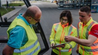 Rozmowa trzech osób w kamizelkach ostrzegawczych: doradztwo z zakresu bezpieczeństwa na miejscu u klienta. Rozmowa trzech osób w kamizelkach ostrzegawczych: doradztwo z zakresu bezpieczeństwa na miejscu u klienta.