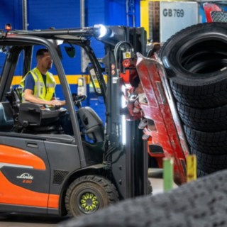 Pracownik Michelin Tyre PLC chwyta stos opon za pomocą chwytaka zamontowanego na wózku widłowym.
