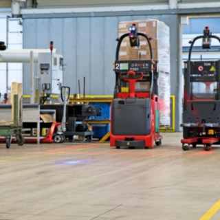 Dwa automatyczne wózki wysokiego podnoszenia L-MATIC transportują towary między linią pakowania a magazynem przepływowym.