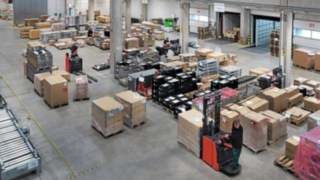 Magazyn logistyczny firmy Simon Hegele z pracownikami sortującymi i transportującymi palety z towarami.
