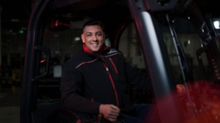 Pracownik Linde Material Handling siedzi w wózku przemysłowym i uśmiecha się do kamery.