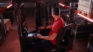 Operator siedzi w ergonomicznej kabinie wózka wysokiego składowania Ri16 firmy Linde MH.