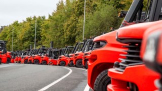 Dużo wózków widłowych marki Linde Material Handling ustawionych w rzędzie na parkingu.