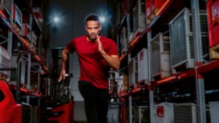 Mężczyzna w stroju sportowym biegnie korytarzem magazynu.