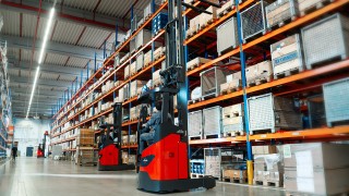 Czerwone wózki widłowe wysokiego składowania Linde reach truck pracujące w alei między wysokimi regałami paletowymi w magazynie