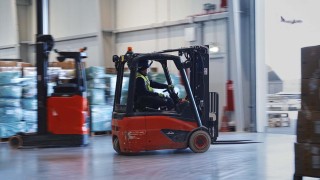 Elektryczny wózek widłowy czołowy Linde sterowany przez operatora przejeżdża obok wózka widłowego reach truck Linde w hali magazynu cargo