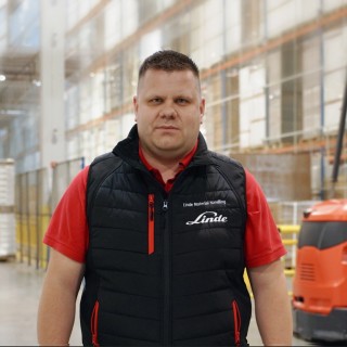 Mateusz Sadowski Lider Sprzedaży Wózków VNA Linde Material Handling Polska, stojący w magazynie na tle wózka widłowego VNA