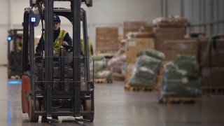 Operator w kasku ochronnym kieruje wózkiem widłowym Linde z widocznym niebieskim światłem ostrzegawczym BlueSpot w magazynie