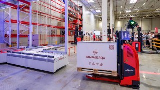 Wózek widłowy AGV transportujący ładunek na tle powierzchni magazynowej z regałami