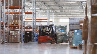 Elektryczny wózek widłowy Linde z operatorem w kamizelce Welcome Airpot Services przewozi paletę w dużym magazynie cargo, obok innych pracowników i wózków